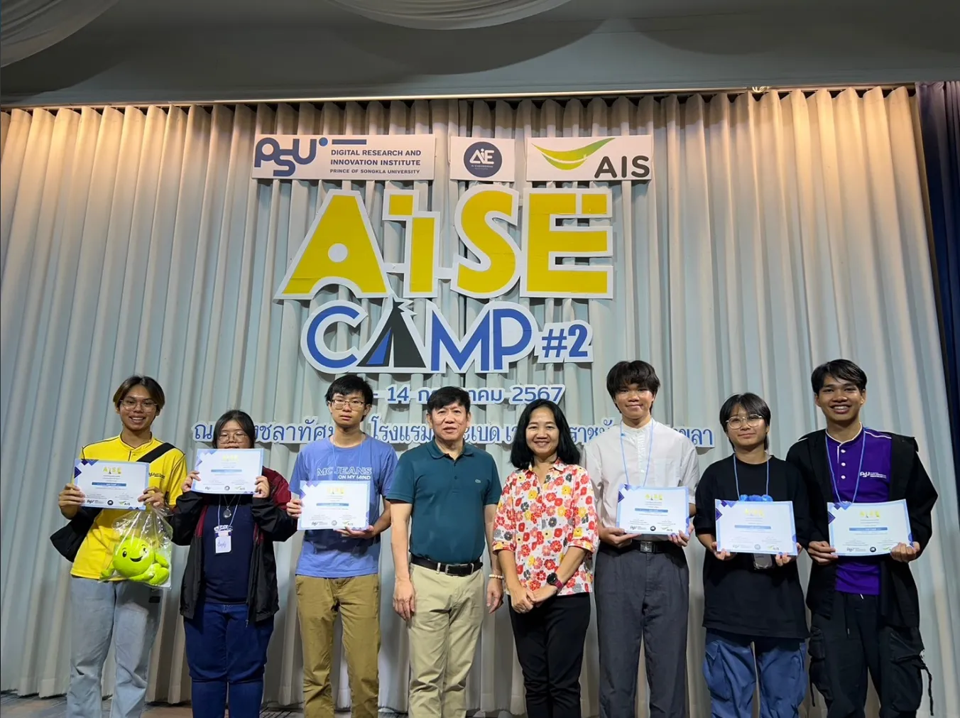 Certificate holders in front of the AiSE CAMP #2 sign